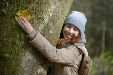 Porträt eines lächelnden Teenagers, der sich in einem herbstlichen Wald an einen Baumstamm schmiegt - LBF02051