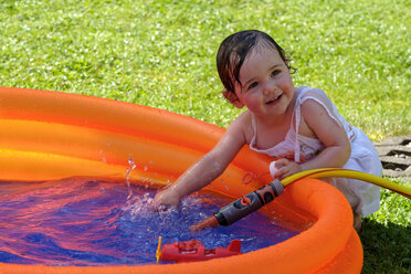 Porträt eines lächelnden kleinen Mädchens, das in einem Planschbecken im Garten mit Wasser planscht - LBF02059