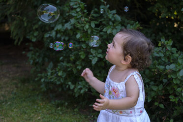 Baby girl watching flying soap bubbles in the garden - LBF02061