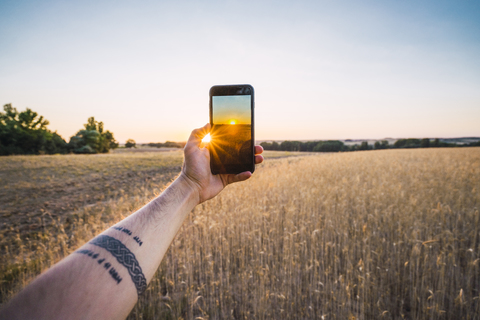 Mann, der mit seinem Smartphone den Sonnenuntergang und die Felder fotografiert, lizenzfreies Stockfoto