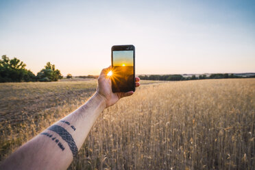 Mann, der mit seinem Smartphone den Sonnenuntergang und die Felder fotografiert - KKAF01810