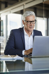 Businessman working in office, using laptop - RBF06593