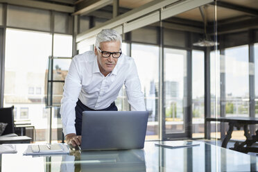 Geschäftsmann steht am Schreibtisch und schaut auf einen Laptop - RBF06598