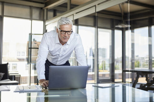 Geschäftsmann steht am Schreibtisch und schaut auf einen Laptop - RBF06598