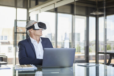 Geschäftsmann sitzt mit Laptop am Schreibtisch und benutzt eine VR-Brille - RBF06599