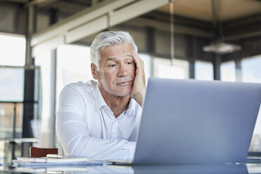 Gelangweilter Geschäftsmann, der am Schreibtisch sitzt und einen Laptop benutzt - RBF06603