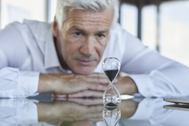 Businessman sitting at desk, watching hourglass - RBF06605