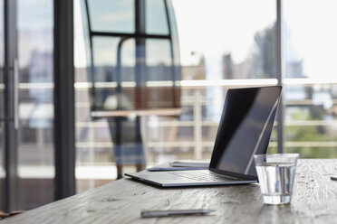 Laptop and glass of water on desk in office - RBF06606