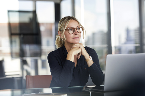 Geschäftsfrau sitzt am Schreibtisch und denkt nach, lizenzfreies Stockfoto