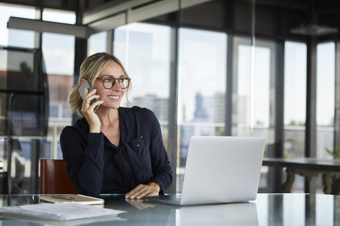 Businesswoman sitting in office, talking on the phone - RBF06644