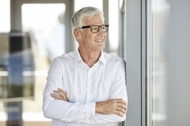 Geschäftsmann in einem Büro, der mit verschränkten Armen am Fenster lehnt - RBF06647