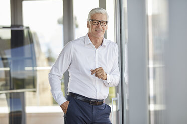 Businessman in office leaning against window, smiling - RBF06652