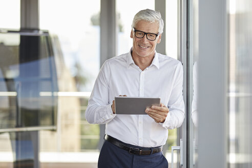 Geschäftsmann lehnt sich an ein Fenster und benutzt ein digitales Tablet - RBF06653