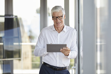 Geschäftsmann lehnt sich an ein Fenster und benutzt ein digitales Tablet - RBF06654