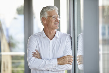 Geschäftsmann in einem Büro, der mit verschränkten Armen am Fenster lehnt - RBF06658