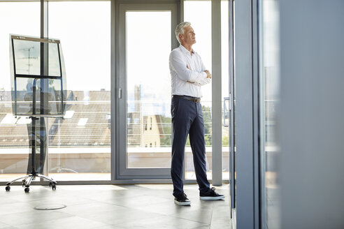 Erfolgreicher Geschäftsmann im Büro stehend, aus dem Fenster schauend, mit verschränkten Armen - RBF06661