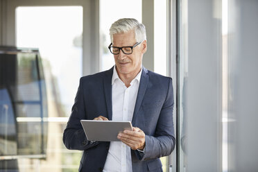 Geschäftsmann, der am Fenster steht und ein digitales Tablet benutzt - RBF06668