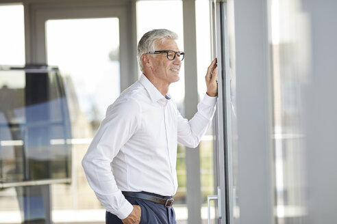 Selbstbewusster Geschäftsmann, der im Büro steht und aus dem Fenster schaut - RBF06671