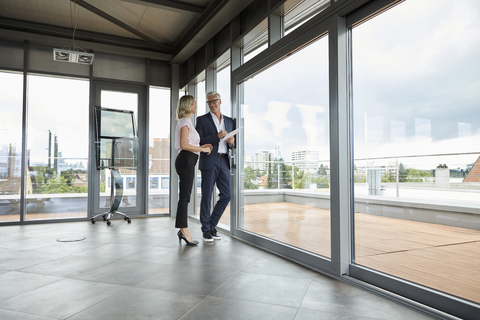 Businessman and woman standing in office, discussing project, holding documents stock photo