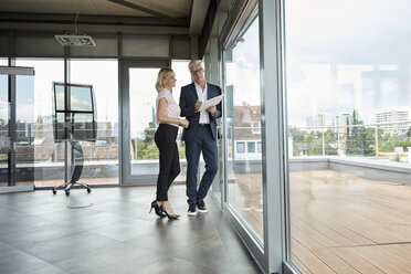 Geschäftsmann und Frau stehen in einem Büro, besprechen ein Projekt, halten Dokumente - RBF06678