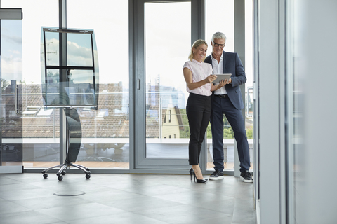 Businessman and woman standing in office, discussing project, looking at digital tabet stock photo