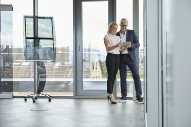 Geschäftsmann und Frau stehen in einem Büro, besprechen ein Projekt und schauen auf eine digitale Tabelle - RBF06680