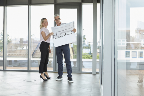 Businessman and woman standing in office, discussing blueprint stock photo