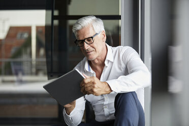 Gelassener Geschäftsmann, der im Büro auf dem Boden sitzt und ein digitales Tablet benutzt - RBF06688