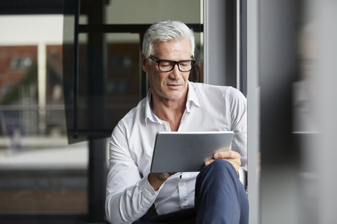 Serene businessman sitting on ground in office, using digital tablet stock photo