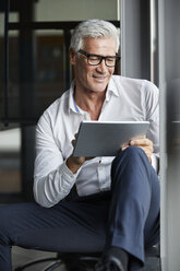 Gelassener Geschäftsmann, der im Büro auf dem Boden sitzt und ein digitales Tablet benutzt - RBF06690