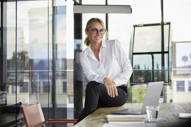 Businesswoman sitting on desk, smiling friendly - RBF06706