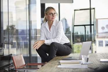 Successful businesswoman sitting on desk, contemplating - RBF06707