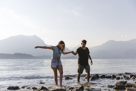 Junges Paar spaziert Hand in Hand am Seeufer, lizenzfreies Stockfoto