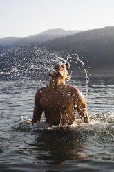 Young man tossing his hair in a lake - MRAF00293