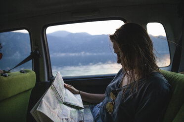 Young woman sitting on backseat in a car looking at map - MRAF00317