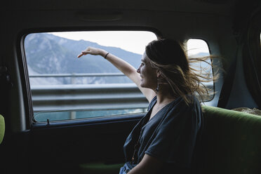 Glückliche junge Frau sitzt auf der Rückbank eines Autos und schaut aus dem Fenster - MRAF00319