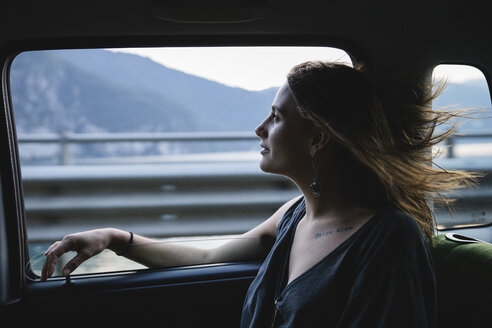 Junge Frau sitzt auf der Rückbank eines Autos und schaut aus dem Fenster - MRAF00320