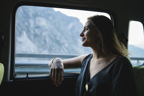 Lächelnde junge Frau sitzt auf der Rückbank eines Autos und schaut aus dem Fenster - MRAF00322