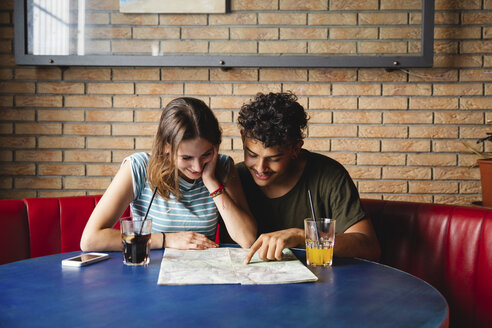 Lächelndes junges Paar sitzt am Tisch in einem Café mit Karte - MRAF00327