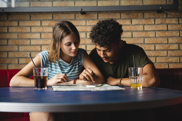 Junges Paar sitzt am Tisch in einem Café mit Landkarte und Mobiltelefon - MRAF00330