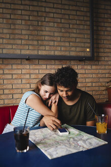 Zärtliches junges Paar am Tisch in einem Café mit Karte und Mobiltelefon - MRAF00331