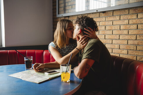 Young couple with map kissing in a cafe - MRAF00333