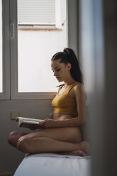 Schöne junge Frau in Unterwäsche liest ein Buch zu Hause - KKAF01818