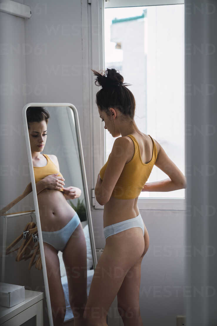 Young woman in underwear at home looking in mirror stock photo