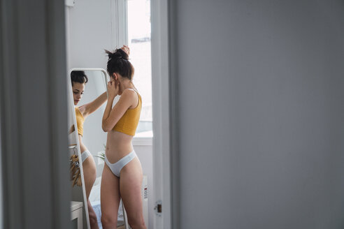 Junge Frau in Unterwäsche zu Hause in den Spiegel schauen - KKAF01825