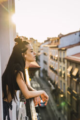 Schöne junge Frau auf Balkon über der Stadt bei Sonnenuntergang - KKAF01835