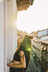 Schöne junge Frau auf Balkon über der Stadt bei Sonnenuntergang - KKAF01842