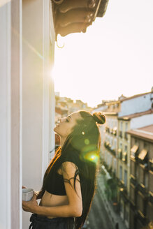 Beautiful young woman on balcony above the city at sunset - KKAF01842