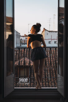Beautiful young woman standing on balcony at sunset - KKAF01846