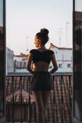 Schöne junge Frau steht auf Balkon bei Sonnenuntergang - KKAF01847